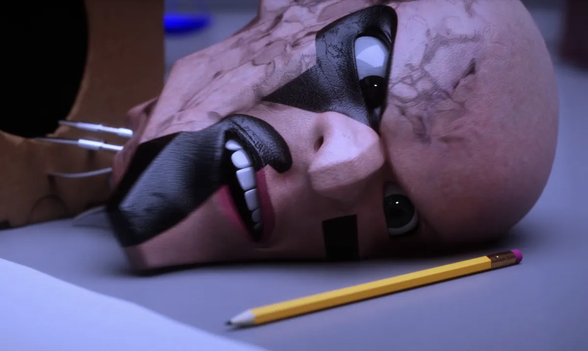 A bald puppet head with a black mask lies on its side on a desk beside a yellow pencil